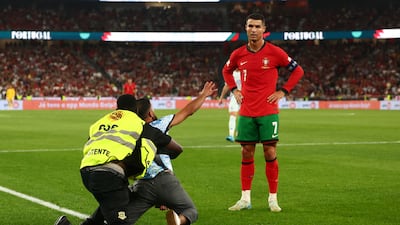 A pitch invader is detained as Cristiano Ronaldo looks on during the Portugal-Scotland match in Lisbon. Reuters